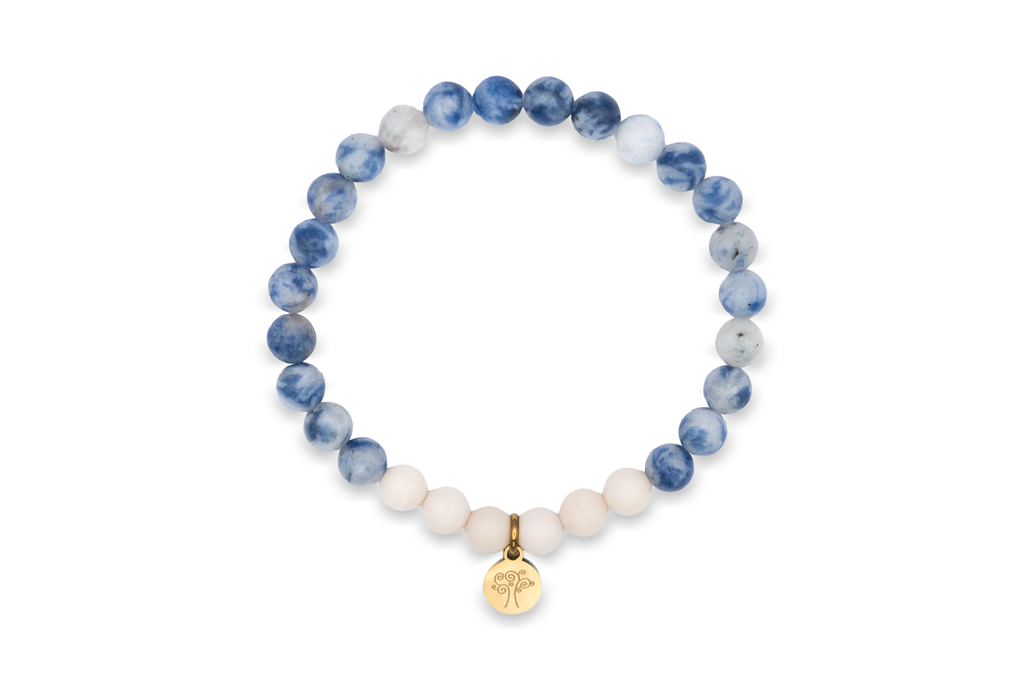 Natursteinarmband „Mondsee“ mit blauen Sodalithperlen, blau-weißen Mikroklineperlen, weißen Marmorperlen und einem goldfarbenen Edelstahl-Anhänger mit vertiefter Baumgravur auf weißem Hintergrund.